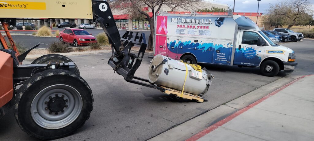 Water heater being lifted into place with a telehandler next to a DMS Plumbing service truck