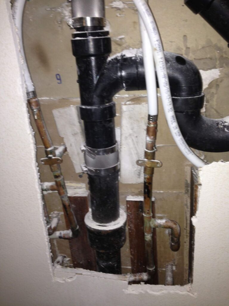 Opened wall showing drain and water supply lines repaired after a hidden leak