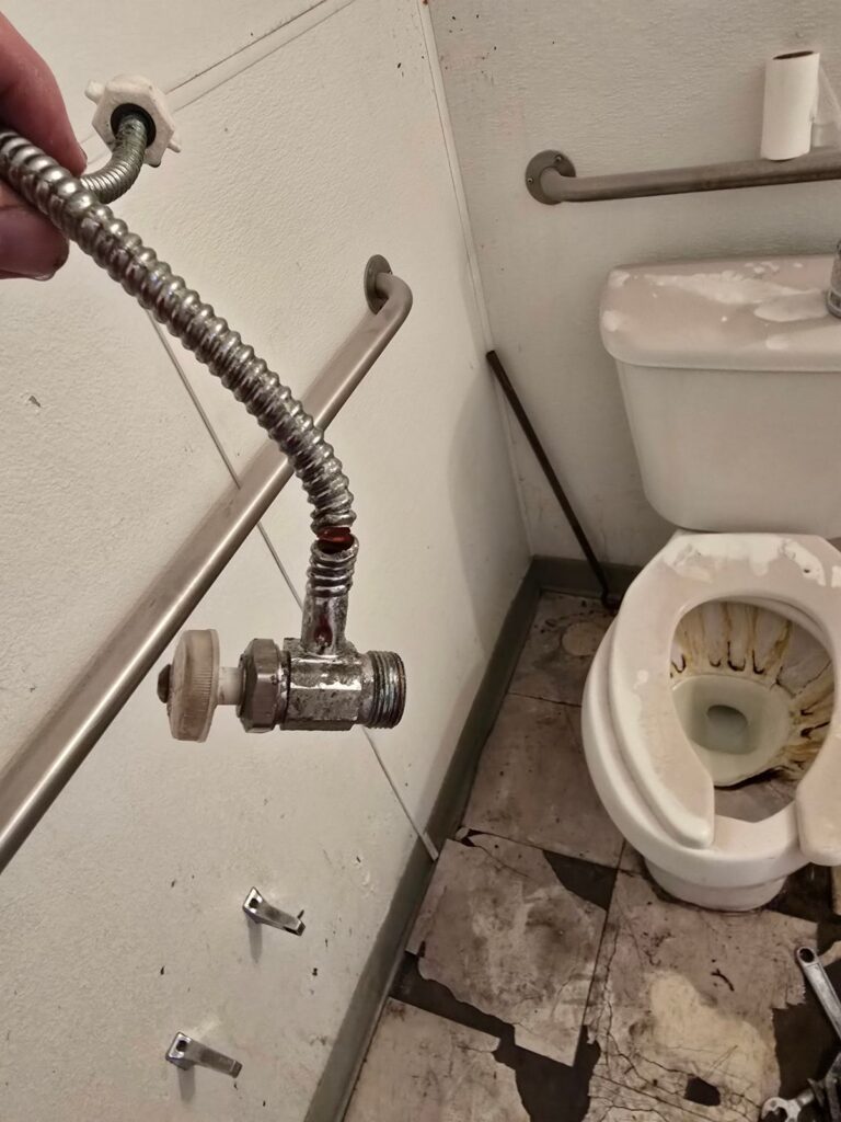 Toilet supply line and shutoff valve being replaced during a toilet repair