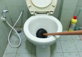 A toilet with the lid up and a wooden stick in it.